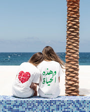 Two people sitting on a tiled ledge by the ocean with palm trees.
