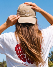 Person wearing a beige cap and white t-shirt with red text outdoors on a clear day